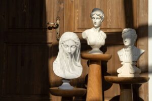 Trois bustes blancs exposés sur des consoles en bois, devant une porte