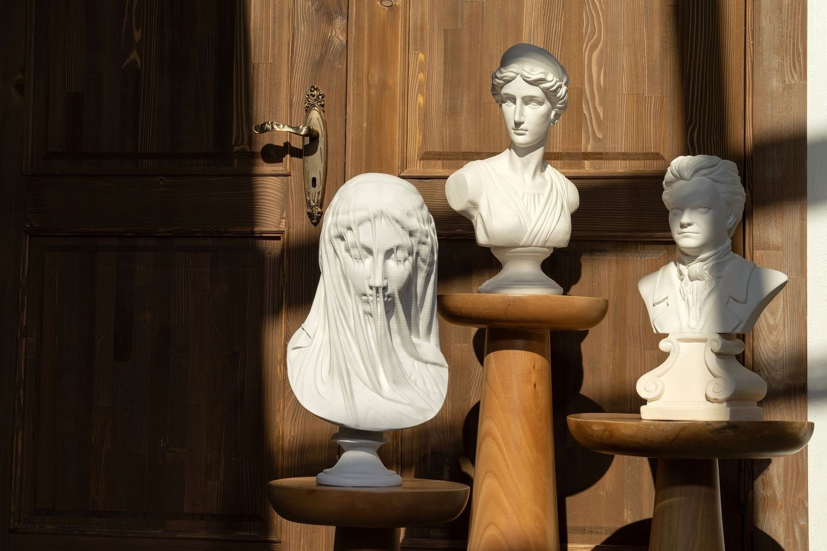 Trois bustes blancs exposés sur des consoles en bois, devant une porte